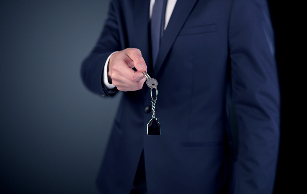 Young businessman hand over keys with empty dark background